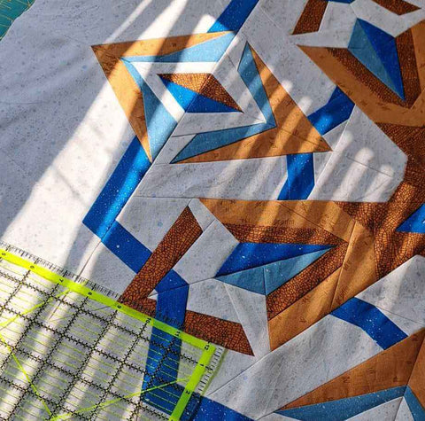 Nesting Phoenix quilt top in the sunshine with a ruler for squaring.