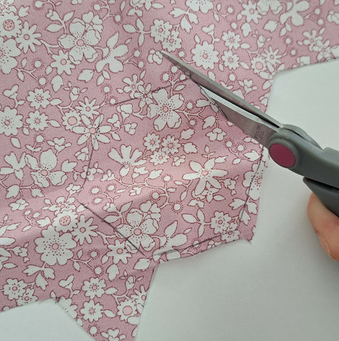 Photo of scissors cutting a pink floral fabric in a hexagon shape for EPP