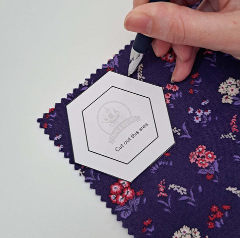 Photo of hand holding pen tracing along the outside of a hexagon template onto floral fabric.