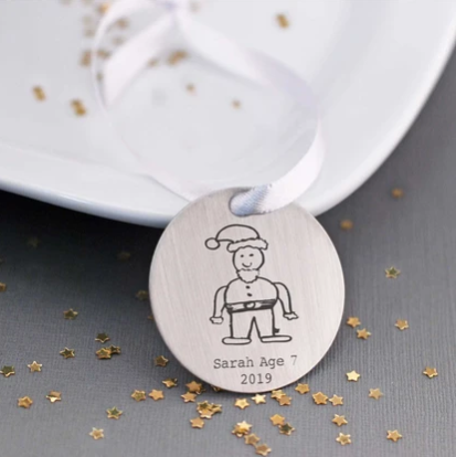Christmas ornament engraved with child’s drawing of Santa, child’s name, child’s age, and year.