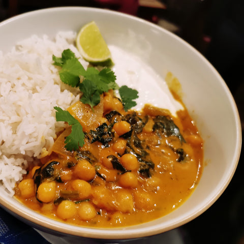 Chickpea curry with vegetables and basmati rice, served in a white bowl with a lime wedge and fresh coriander leaves