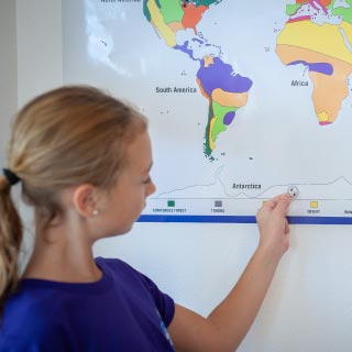 young girl placing animal track sticker on color-coded habitat map