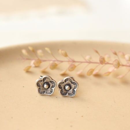 The mini cactus flower silver dot earrings styled on a tan plate with dried grass