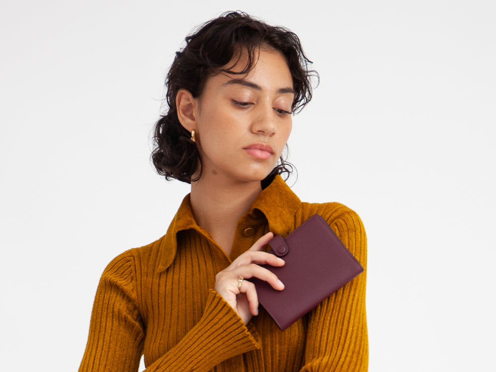 a girl in a mustard yellow top hold a burgundy bifold wallet