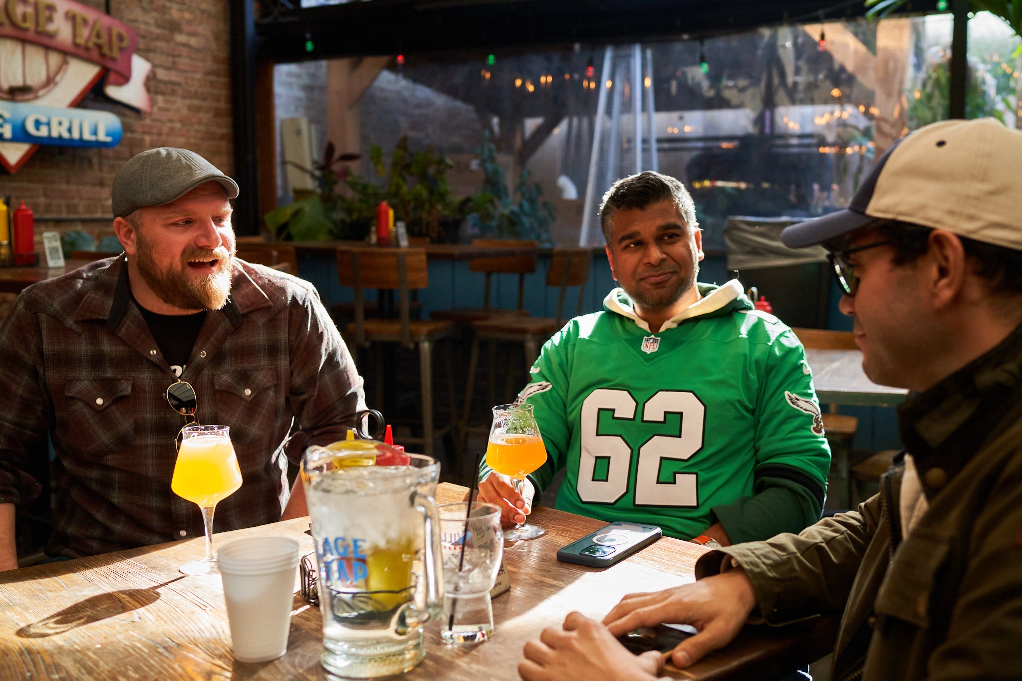 Three men sitting at a table with water and beer in mid-conversation