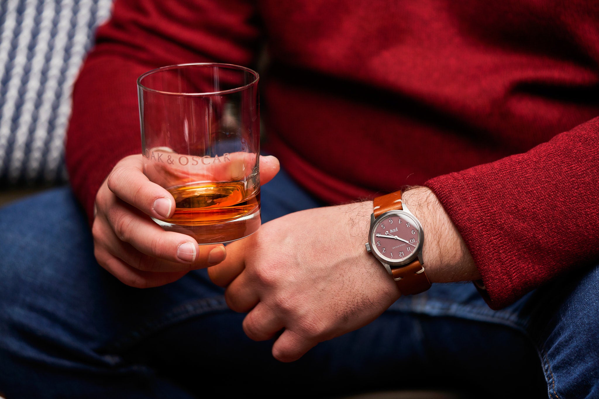 Image of man wearing red sweater holding glass of bourbon while wearing the Olmsted FEW edition with a salmon dial.