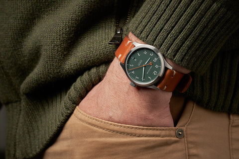 Oak & Oscar Olmsted green dial field watch on leather strap. hand in pocket with chunky green sweater.