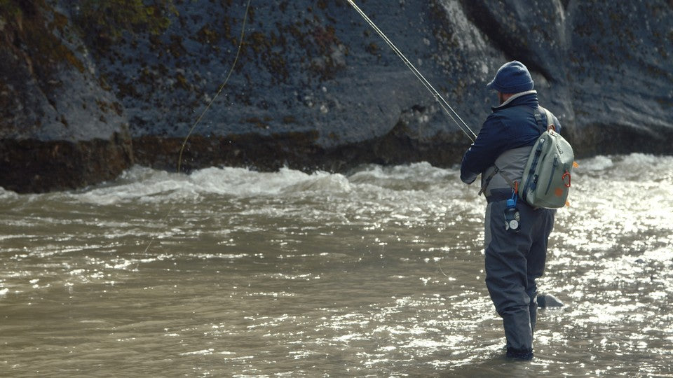 Owner of Oak & Oscar Chase Fancher fishing in a river cutting through the swiss alps