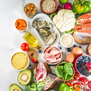 Healthy foods including meats, vegetables, nuts, fish and fruits laid out on table in small bowls