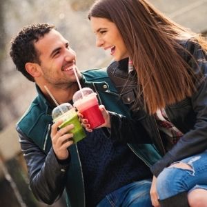 Man and woman holding green and red drinks and smiling