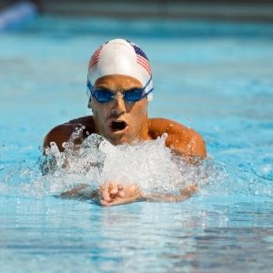 Man wearing USA Swim cap and goggles swimming breaststroke in a pool