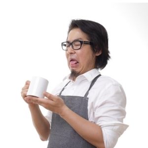 Man wearing apron holding a mug reacting to a bad taste