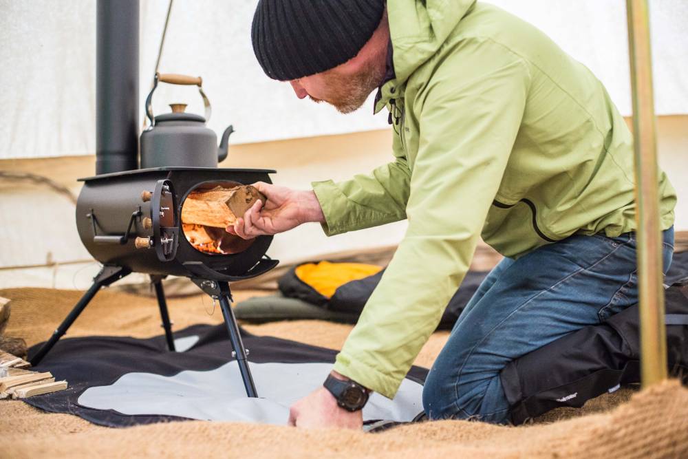 Man adding fuel to a Frontier woodburning stove in a bell tent