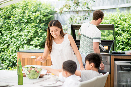 family outside, grilling and sitting at table in outdoor kitchen