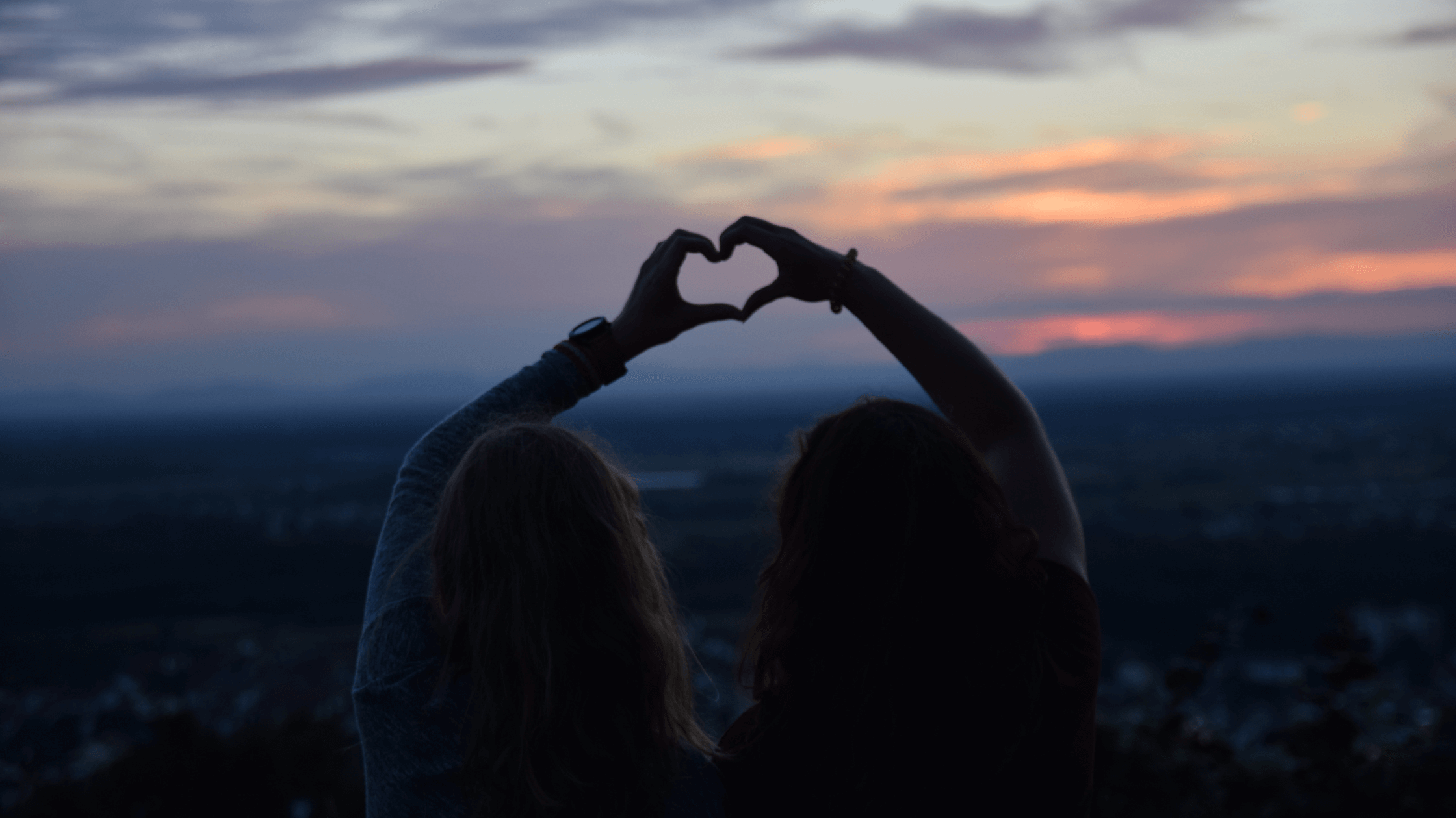 Two people making a heart with their hands as they support, love and help each other through tough times.