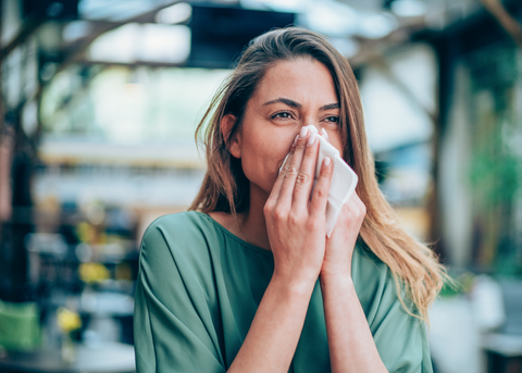 Una mujer estornuda, destacando los efectos de las alergias estacionales en el cuidado bucal y la salud dental.