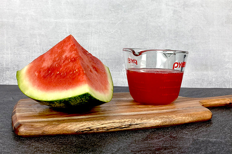 Wedge of watermelon next to a measuring cup filled with one cup of watermelon juice.