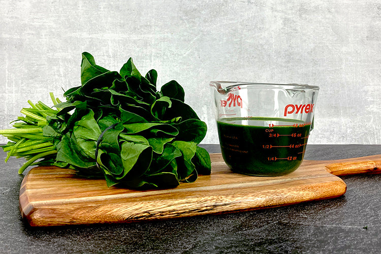 One and a half bundles of spinach next to a measuring cup filled with one cup of spinach juice.