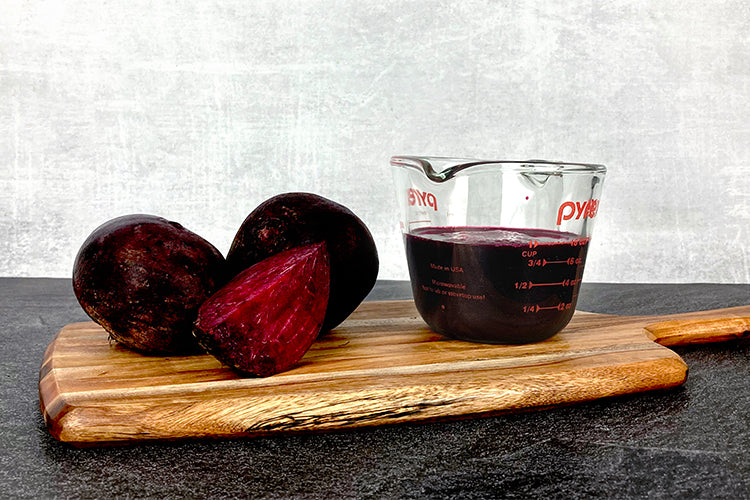 Two and a quarter beets next to a measuring cup filled with one cup of beet juice.