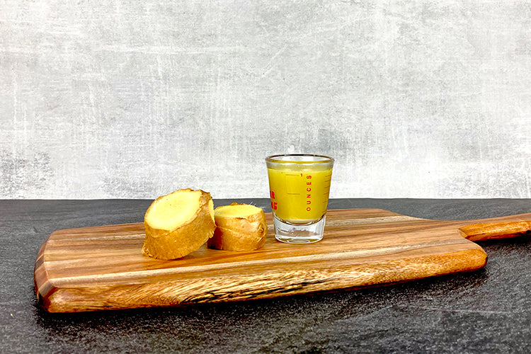 Two slices of ginger next to a one ounce shot glass filled with ginger juice.