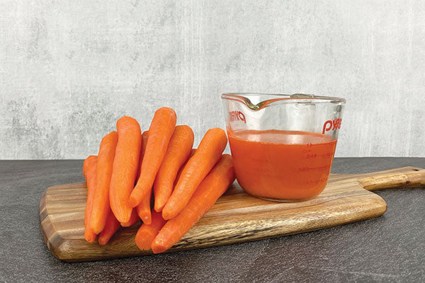 Carrots next to a measuring cup filled with one cup of carrot juice.