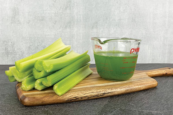 Celery sticks next to a measuring cup filled with one cup of celery juice.