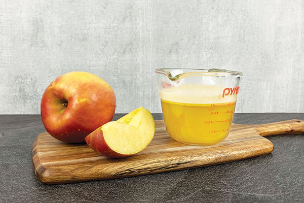 An apple and an apple slice next to a measuring cup filled with one cup of apple juice.