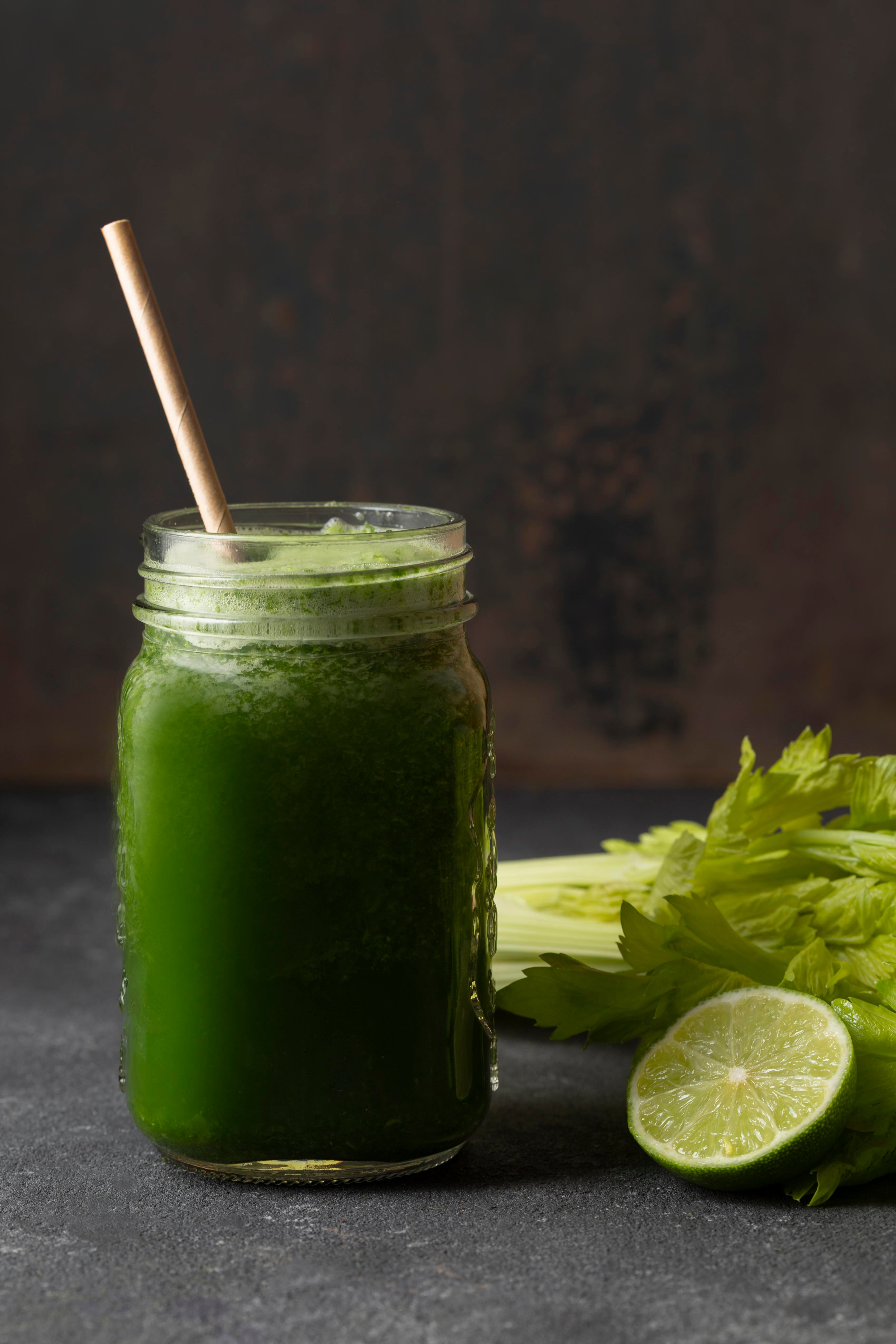 green juice in a jar next to celery and half a lime