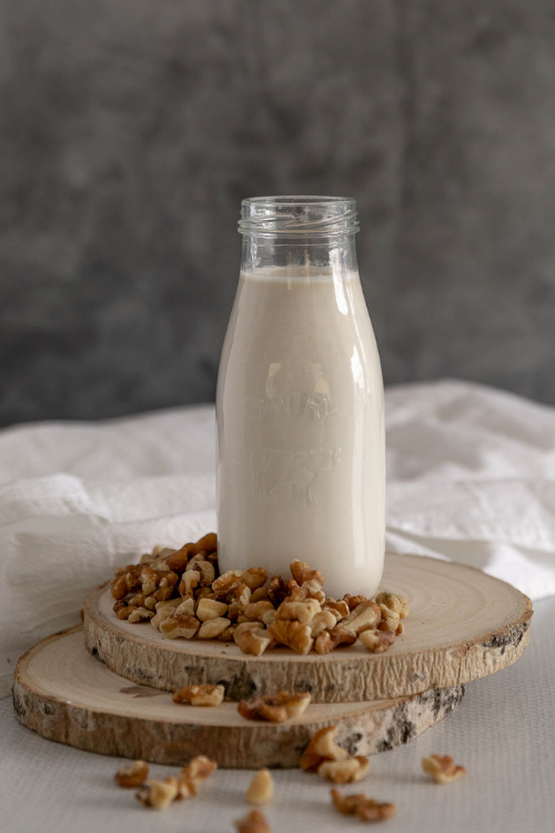 Bottle of walnut milk surrounded by scattered walnut pieces