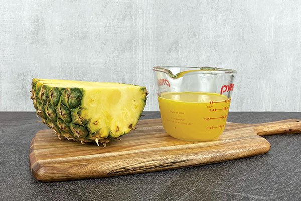 Half a pineapple next to a measuring cup filled with one cup of pineapple juice.