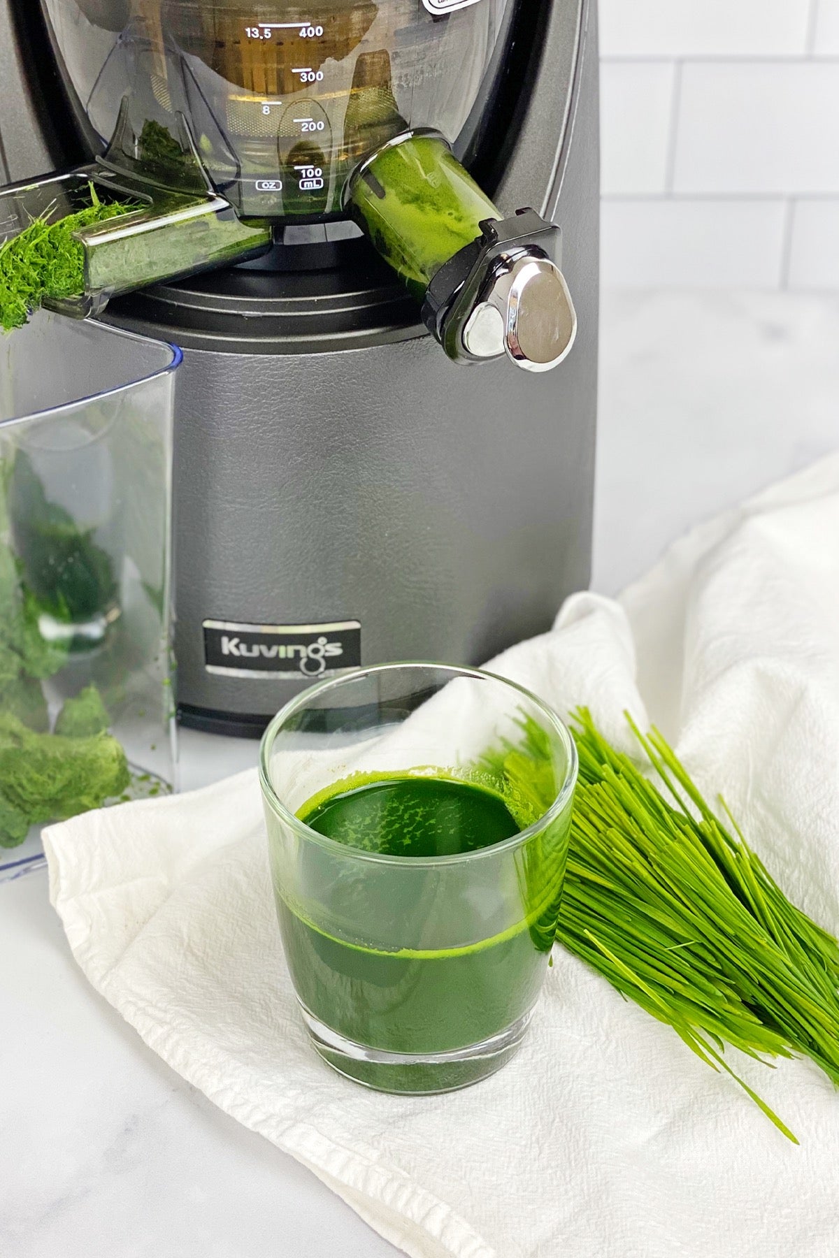 green juice in glass cup with grass, gray juicer