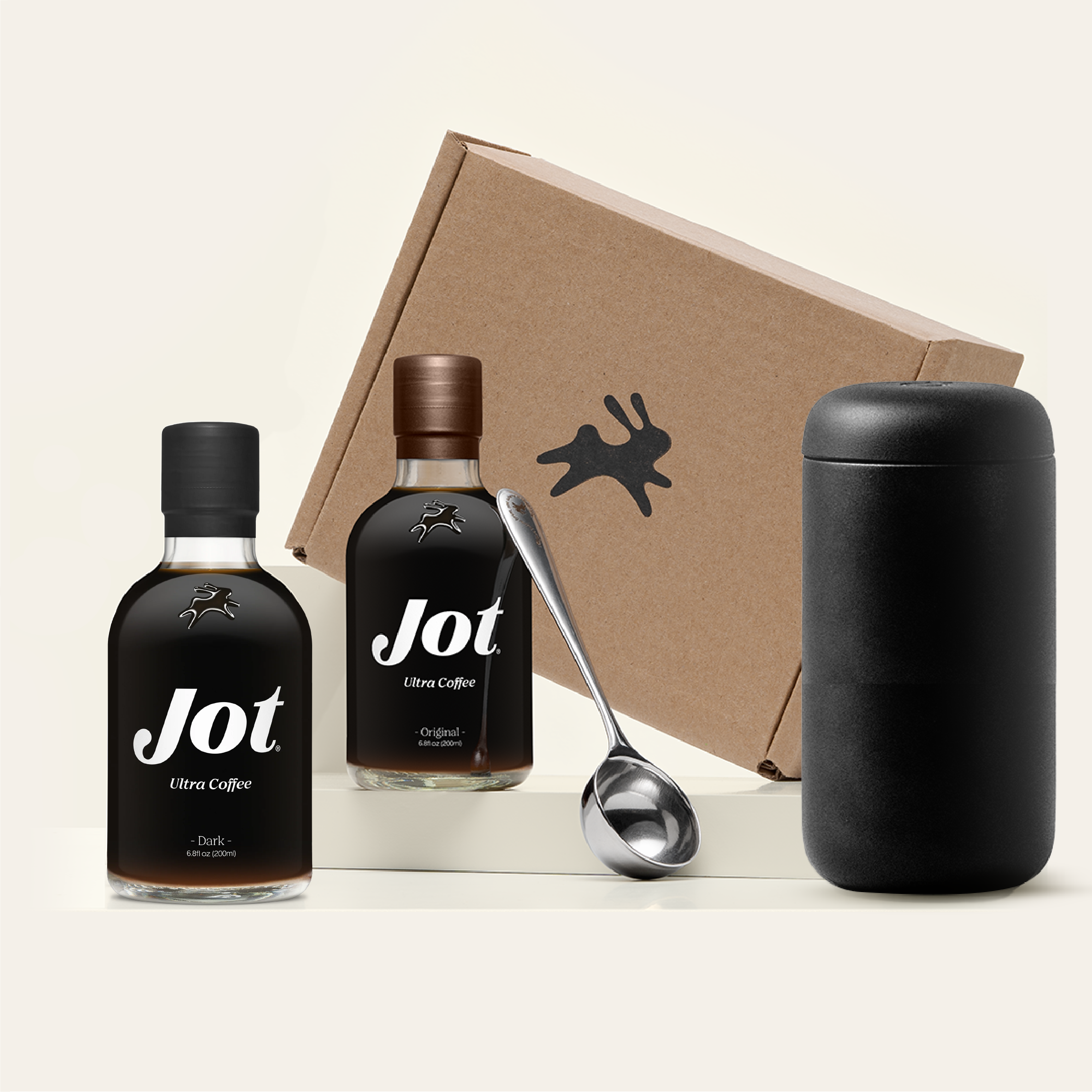 Two bottles of Jot ultra coffee, a spoon, and a portable cup next to a cardboard box.