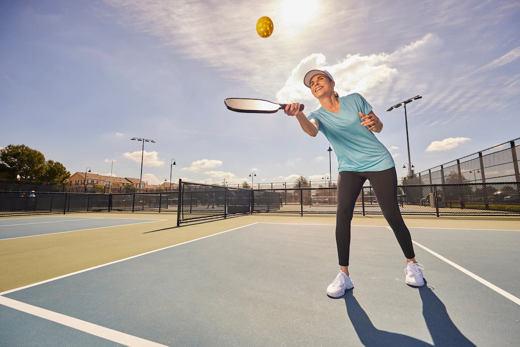 Woman playing pickleball on an outdoor court, reaching for the ball with her paddle.