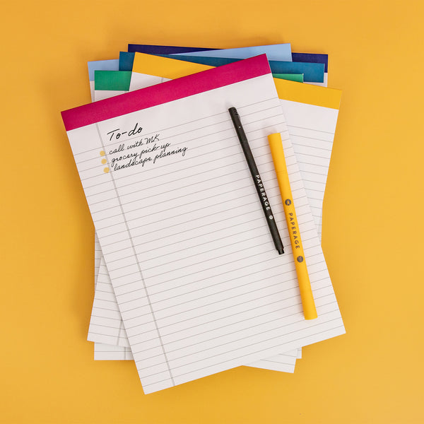A Stack of PAPERAGE Legal Pads and Pens on yellow background