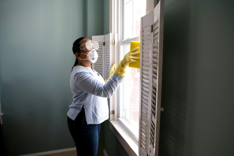 A photo of a woman with mask, gloves and safety goggles cleaning a window using a sponge.