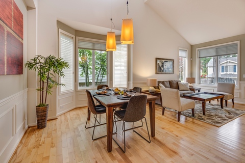 a living room is staged with a dining table and chairs, chandelier, couch and chairs, a plant, and artwork