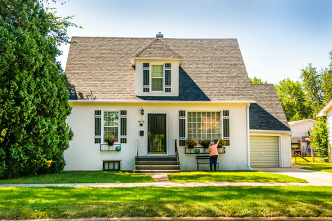 Woman waters plants outside her white two story home in the front yard