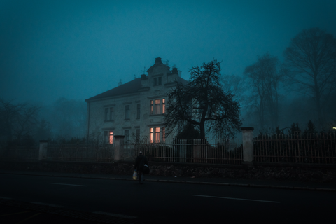 A scary old house with a man standing outside the gate.