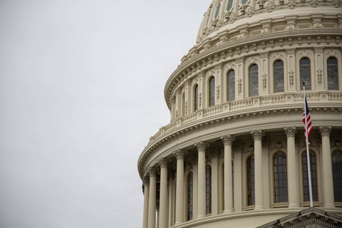 Capitol building with flag against blue sky