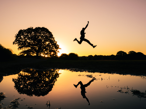 Silhouette of a person jumping across a pond of water