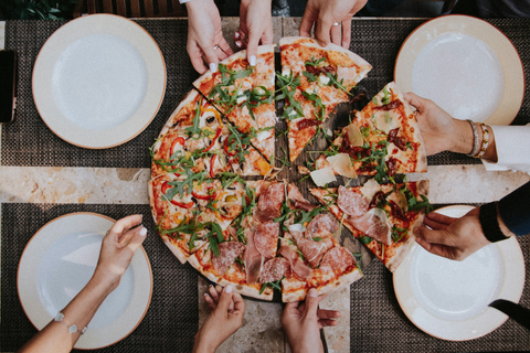 A whole size of pizza with people's hands reaching for a slice