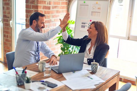 Man and woman high-five will sitting at a desk with a computer and business papers