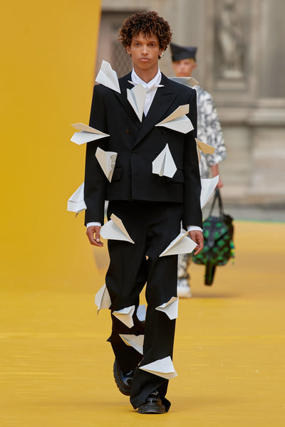 Model wears a black suit with 3D paper aeroplane embellishments at Louis Vuitton's SS23 presentation for Paris Fashion Week