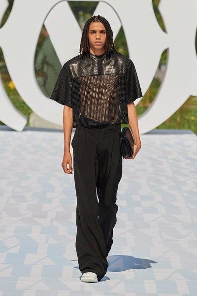 Model wears a cropped mesh and leather T-shirt with relaxed trousers at AMIRI's SS23 presentation for Paris Fashion Week