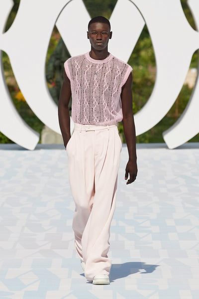 Model wears a pink semi-sheer tank top with wide-leg pink tailored trousers at AMIRI's SS23 presentation for Paris Fashion Week