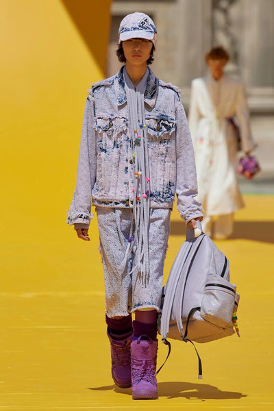 Model wears a lilac denim jacket with cropped lilac jeans and dark purple suede boots at Louis Vuitton's presentation for SS23