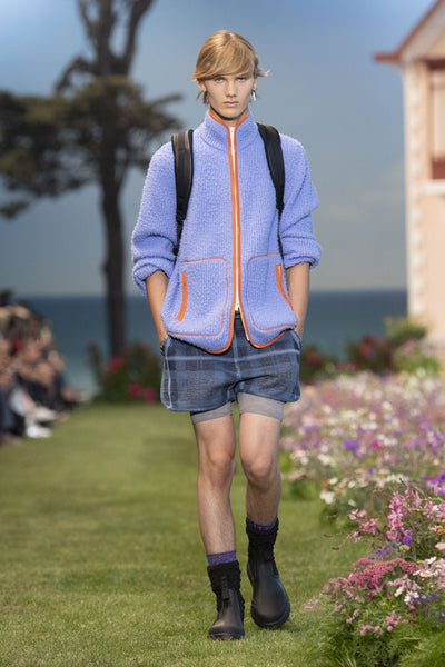 Model wears a purple flee jacket, tartan shorts and rubber rain boots at Dior's SS23 presentation for Paris Fashion Week