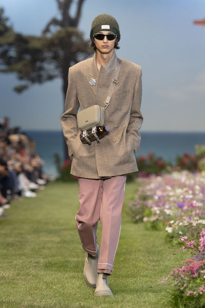 Model wears a beige tailored jacket, pink tailored trousers and rubber rain boots with a cross-body bag at Dior's SS23 presentation for Paris Fashion Week