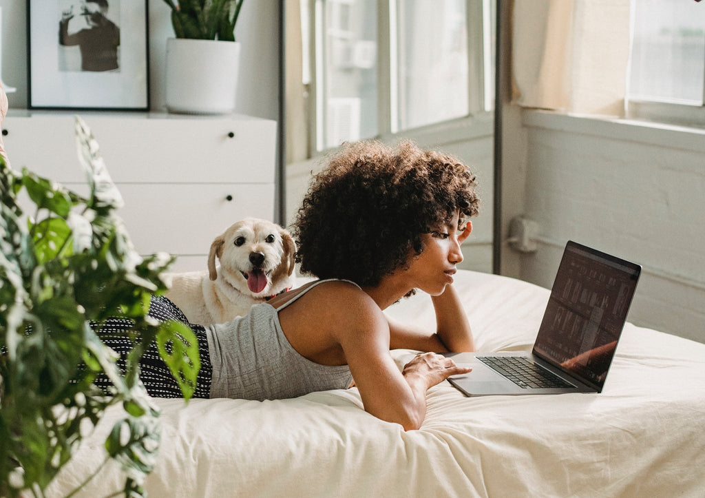 A black woman lying on her back, with her dog beside her, while watching anime using her laptop. 