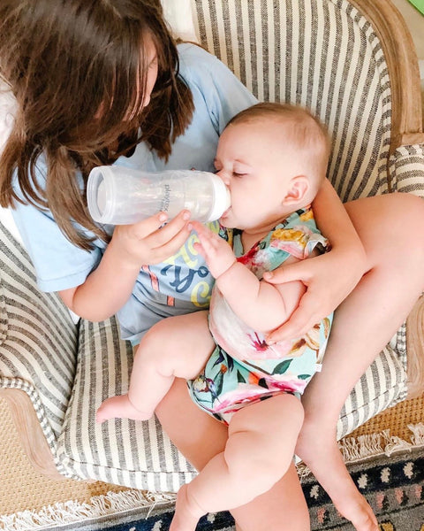 Woman bottle feeding, baby wearing Posh Peanut